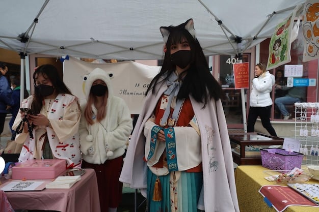 A photo of an artist alley at an anime convention, showing various vendors selling fan-made art prints, keychains, and other merchandise. The artists are interacting with attendees, and the atmosphere is lively and creative.