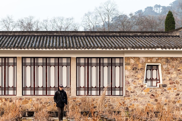 A serene photo of Bukchon Hanok Village in Seoul, South Korea, showcasing traditional Korean houses with tiled roofs and narrow alleyways. A woman dressed in hanbok is walking through the village, enjoying the historic atmosphere, set against a backdrop of lush green hills and modern buildings in the distance.