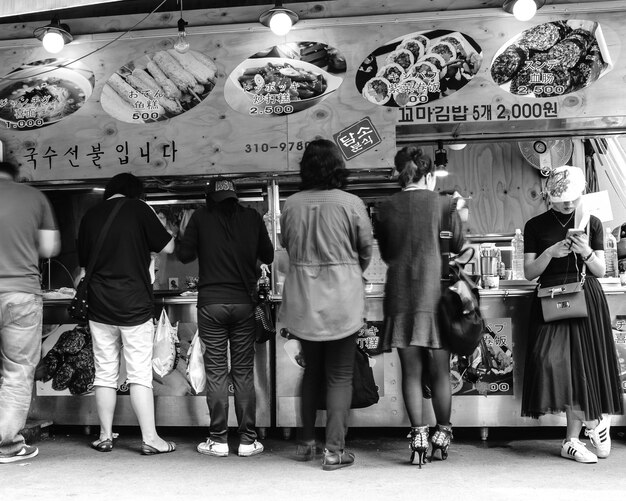 A vibrant photo of a bustling street food market in Myeongdong, Seoul, South Korea, with stalls displaying a variety of Korean street foods such as tteokbokki, Korean fried chicken, and bungeoppang. Tourists are seen sampling the foods and enjoying the lively atmosphere.