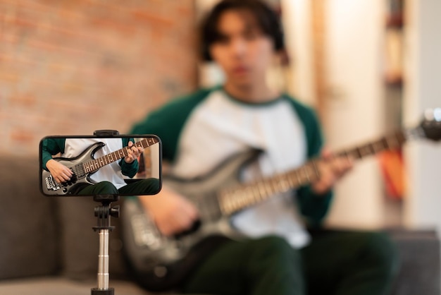 A young musician is recording a video of themselves singing and playing guitar in their bedroom. The room is decorated with posters and instruments, showcasing their passion for music. The scene is intimate and personal, reflecting the DIY nature of TikTok music creation.